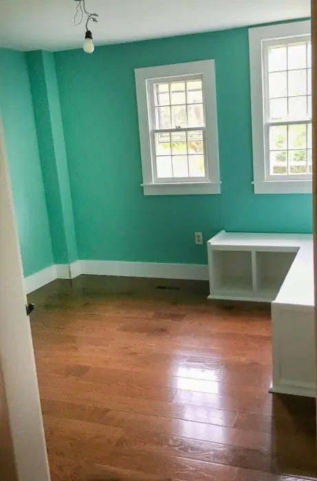 Bright turquoise room with white windows and hardwood floors.
