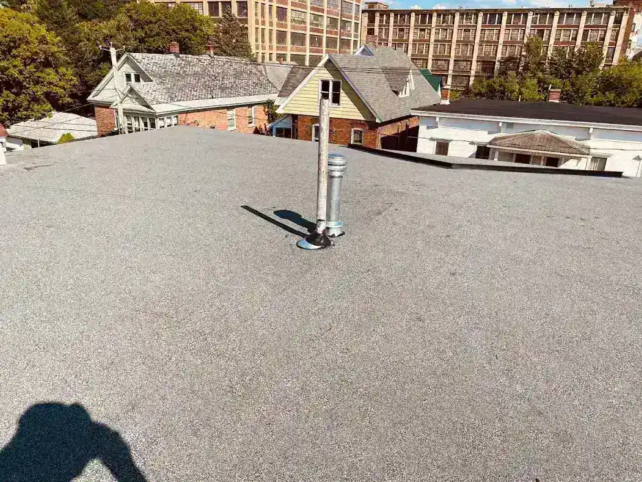 Flat gravel roof with a metal vent pipe and buildings.