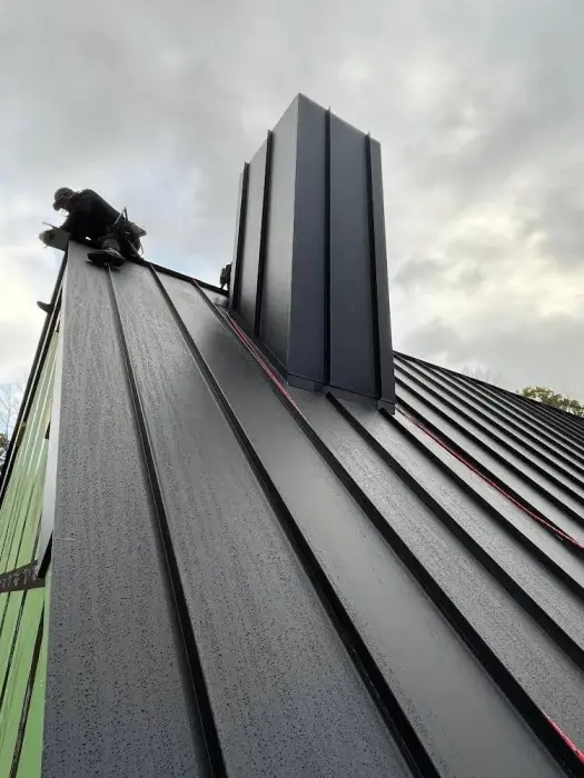 Roofer installing black standing seam metal roofing.