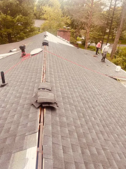 Two roofers working on a residential shingle roof.